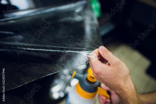 Worker hands installs car paint protection film wrap.