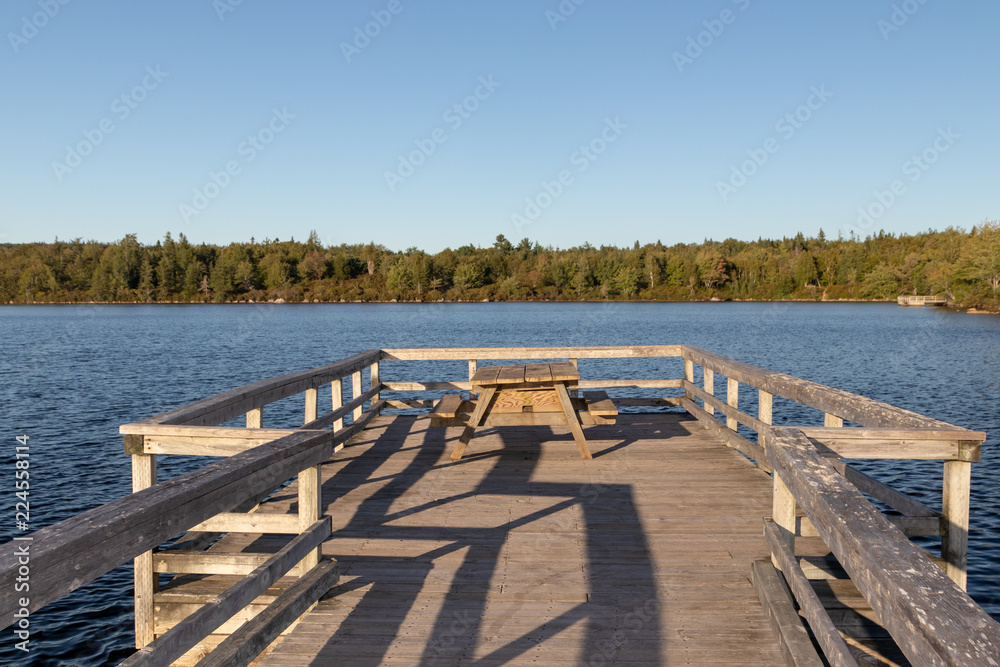 Wooden pier on lake at sunset with picnic table.