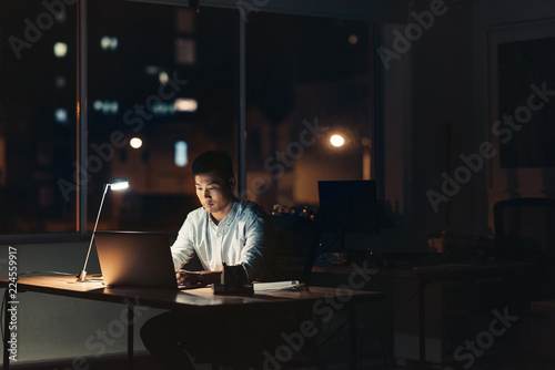 Young Asian businessman working overtime in a dark office photo