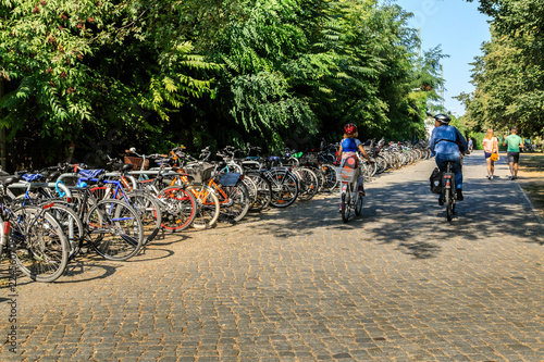 Fototapeta Naklejka Na Ścianę i Meble -   Zwei Radfahrer fahren an einer Reihe geparkter Fahrräder vorbei