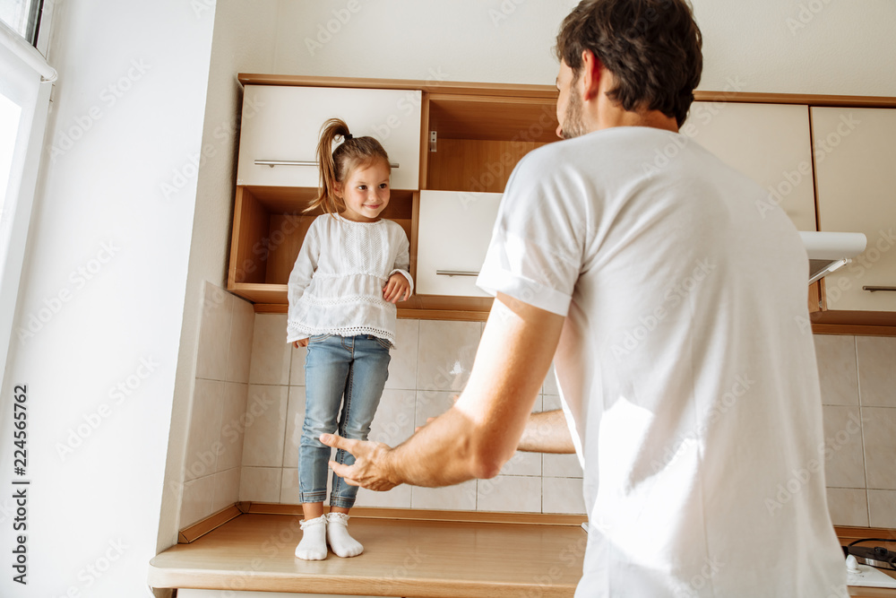 Fototapeta premium Family. Fun. Parenthood. Dad and his little daughter are playing in the kitchen at home