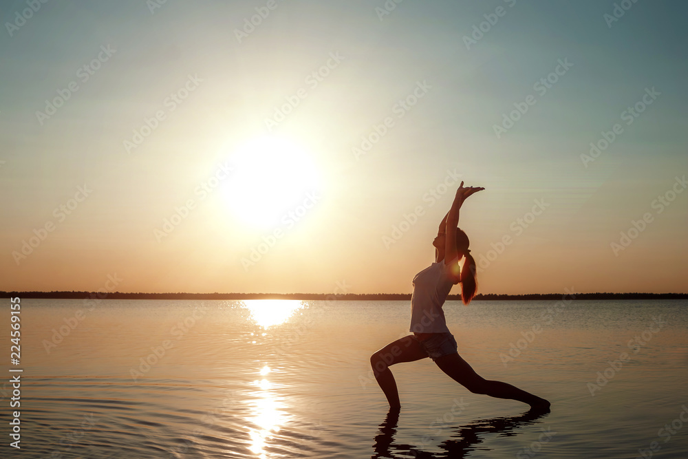 Young girl silhouette, yoga on nature, on a background of a lake and beautiful sunset. Fresh air, healthy way of life, pleasure, pacification.