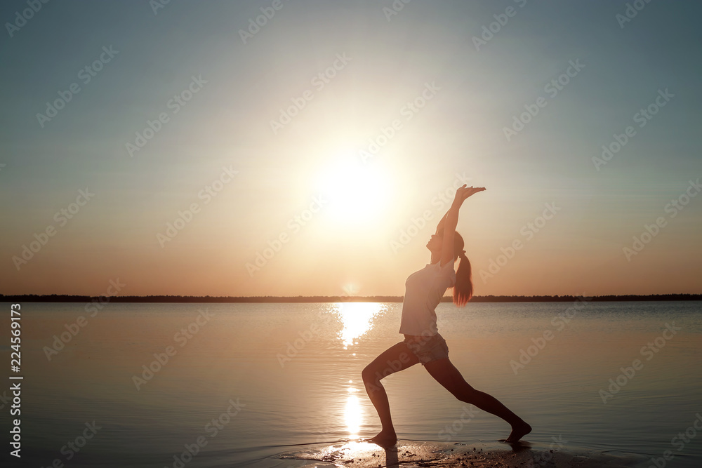 Young girl silhouette, yoga on nature, on a background of a lake and beautiful sunset. Fresh air, healthy way of life, pleasure, pacification.
