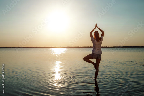 Young girl silhouette  yoga on nature  on a background of a lake and beautiful sunset. Fresh air  healthy way of life  pleasure  pacification.