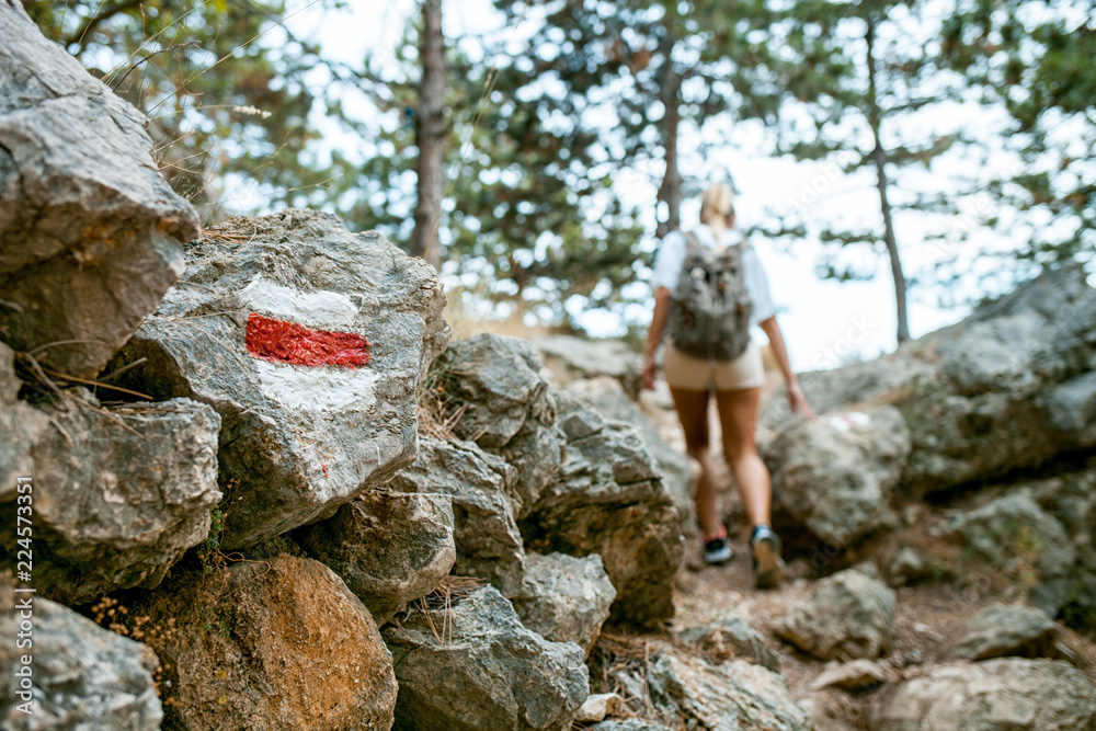Hiking trail sign on rock and tourist woman walking on path Hiking trail sign on rock and tourist woman walking on path