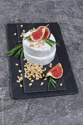 Gourmet appetizer of white brie cheese or camembert with fresh figs, pine nuts, honey and rosemary spice on wooden board