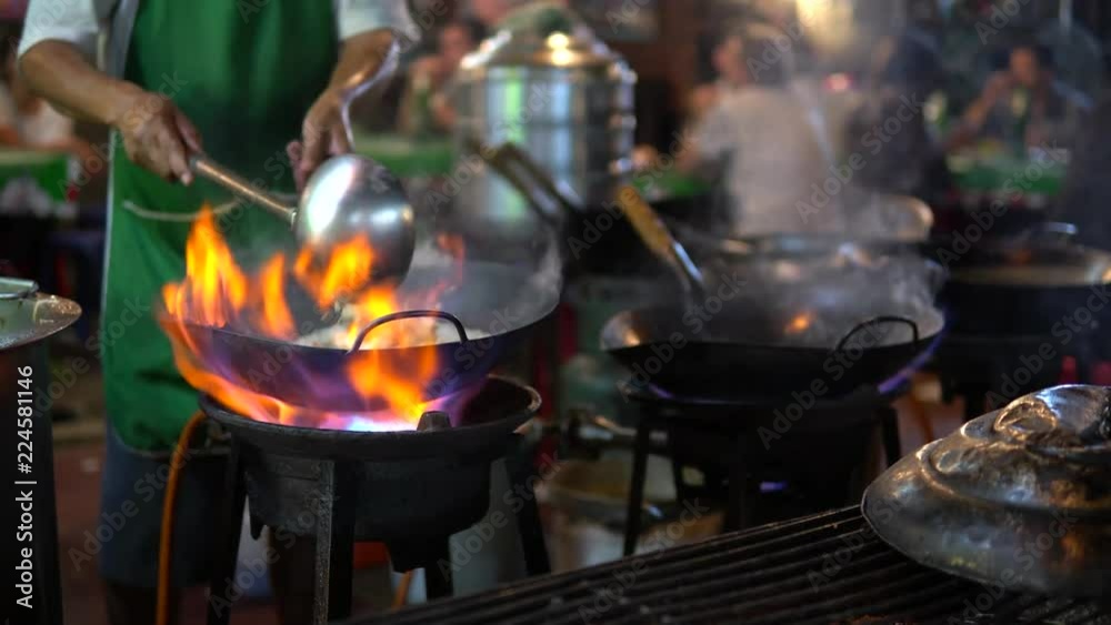 Chef cooking stir fried in a frying pan with chilli peppers,oyster sauce,oil on hot fire from gas in kitchen.Traditional Delicious Thai food.Business,healthy food concept.