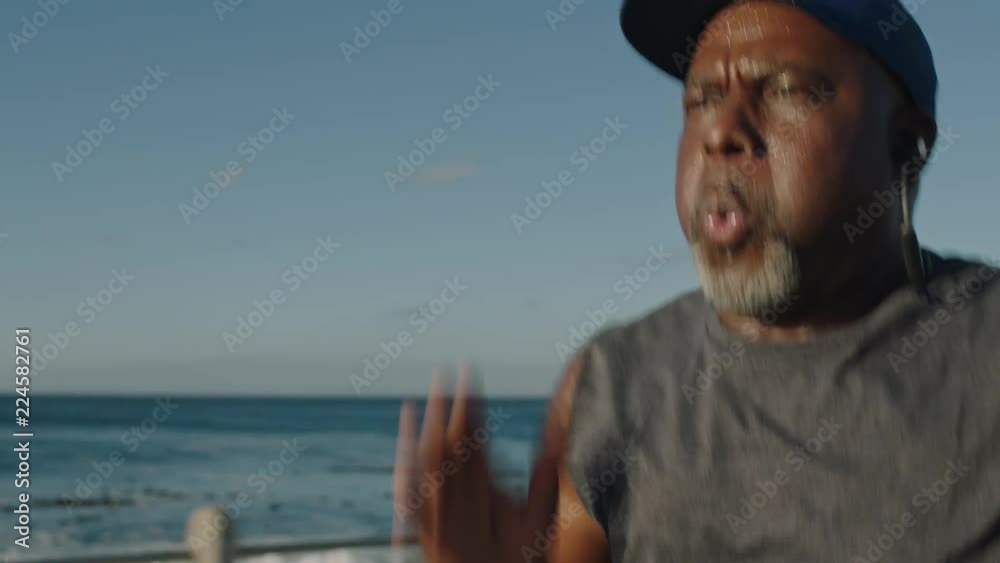 overweight african american man running black male runner exercising jogging healthy fitness workout lifestyle in ocean seaside background at sunrise listening to music