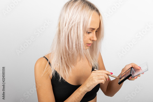 Slender girl with blond hair in a black t-shirt lowered the eye brush in the shade on a white background