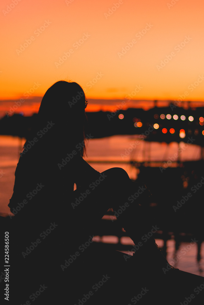 Silhouette of girl at sunset, looking at the harbor