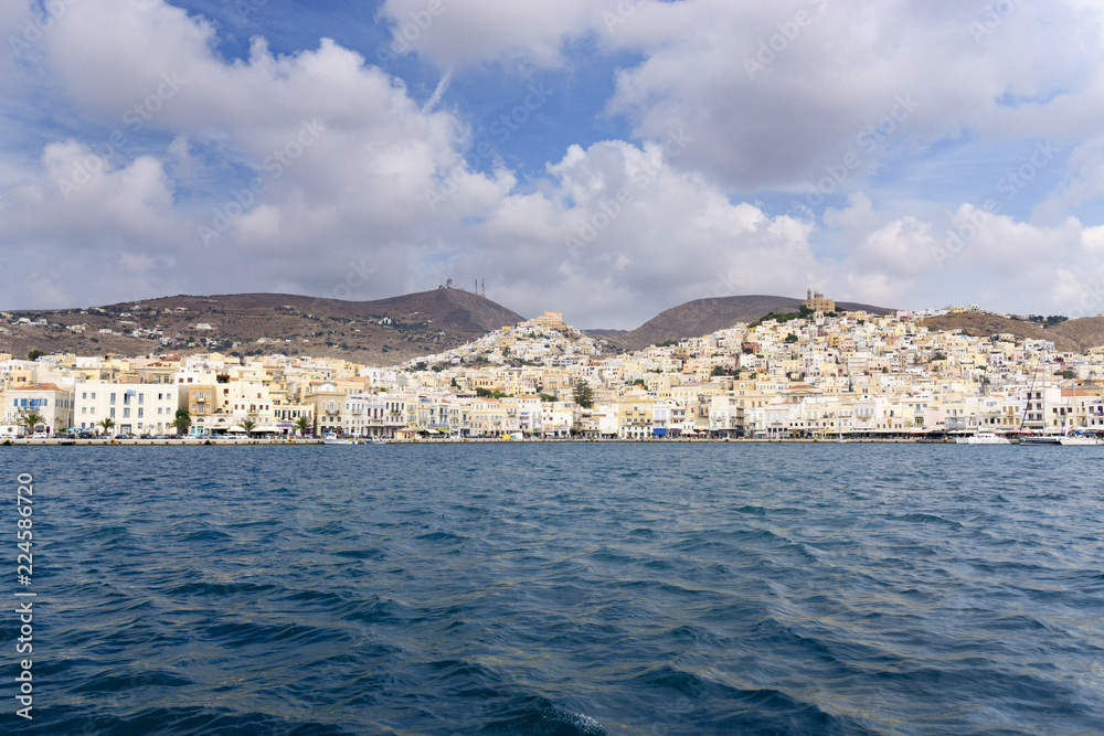 Beautiful view of Ermoupolis city port on Syros island, Greece. Sunny day, dark Aegean sea, cyan sky with clouds and seafront architecture