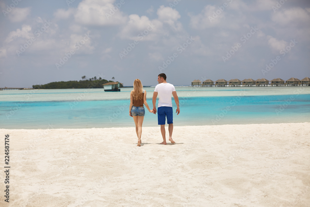 Back view of couple holding hands and walking to the blue ocean lagoon on Maldives at luxury spa resort. Travel and honeymoon concept.