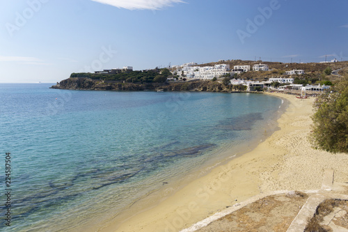 Colorful sandy beach with azure water and local white buildings. Agios Stefanos Beach of Mykonos island  Greece.