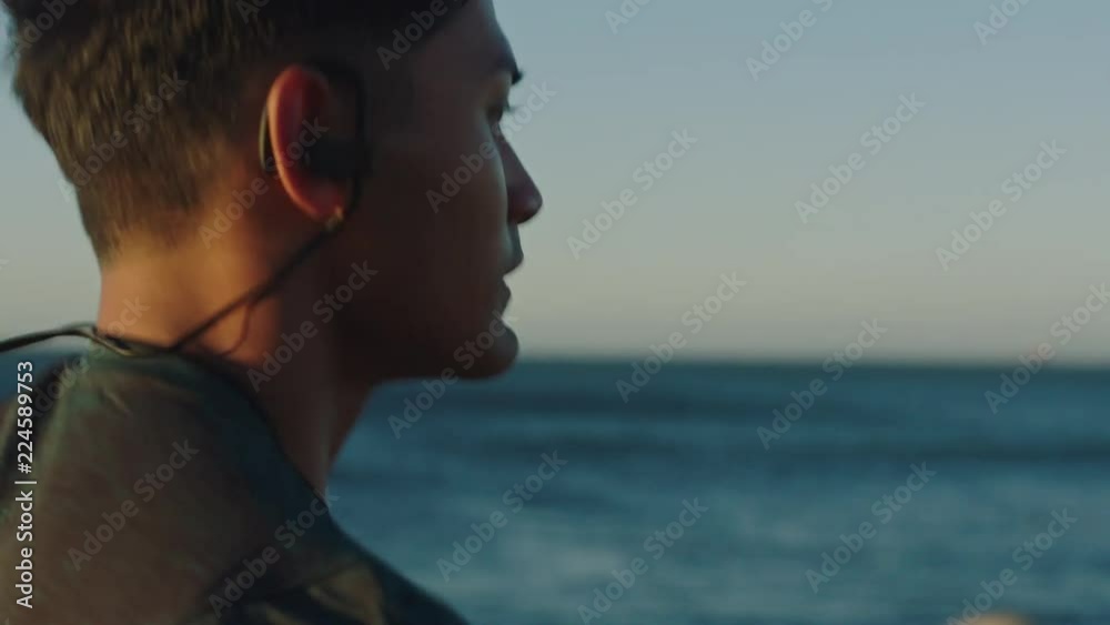 fit young man running athlete runner training tough cardio exercise workout on calm ocean seaside run wearing earphones at sunset close up