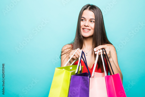 Portrait of an excited beautiful girl wearing red dress and sunglasses holding shopping bags isolated over blue background