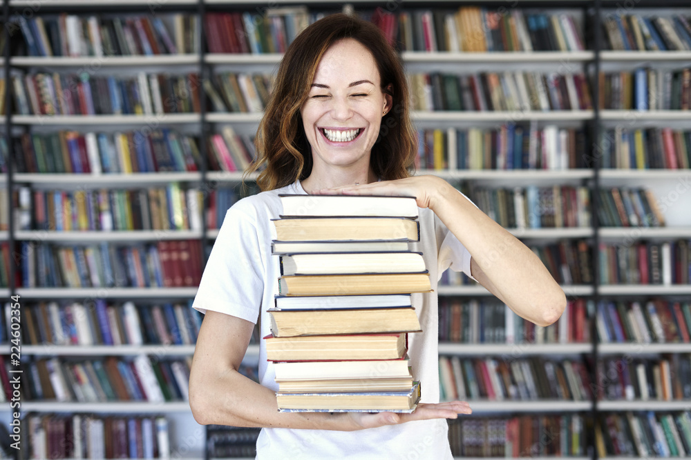 Woman model college student with books at library holds bunch of books, laughs looks smart, smiling to camera. Woman model college student with books at library holds bunch of books, laughs looks smart, smiling to camera.