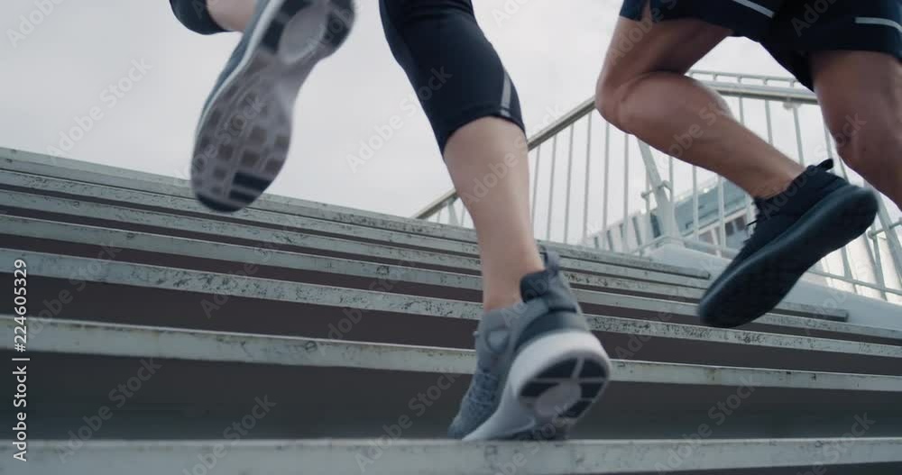 two athletic runners legs running up stairs friends training together in urban city doing intense cardio exercise close up