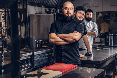Team of professional bearded cooks dressed in uniforms standing in kitchen.