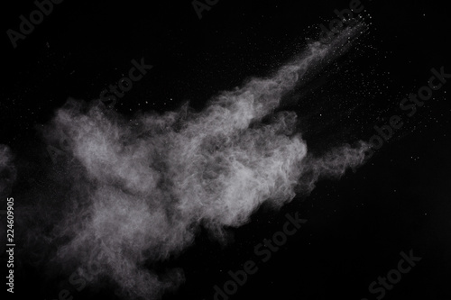 Freeze motion of white dust explosion on black background. Stopping the movement of white powder on dark background. Explosive powder white on black background.