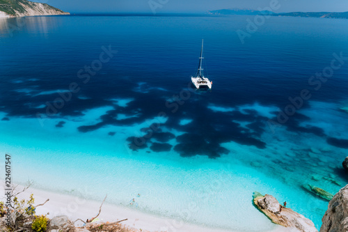 White catamaran yacht drift on clear azure water surface in calm blue lagoon with transparent water and dark pattern on bottom