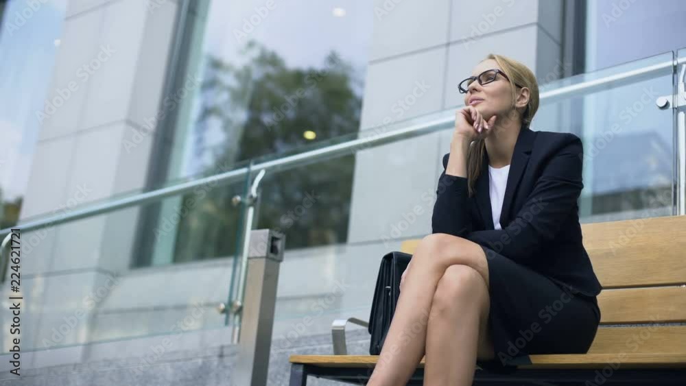 Female entrepreneur sitting on bench, smiling, rejoicing at successful day