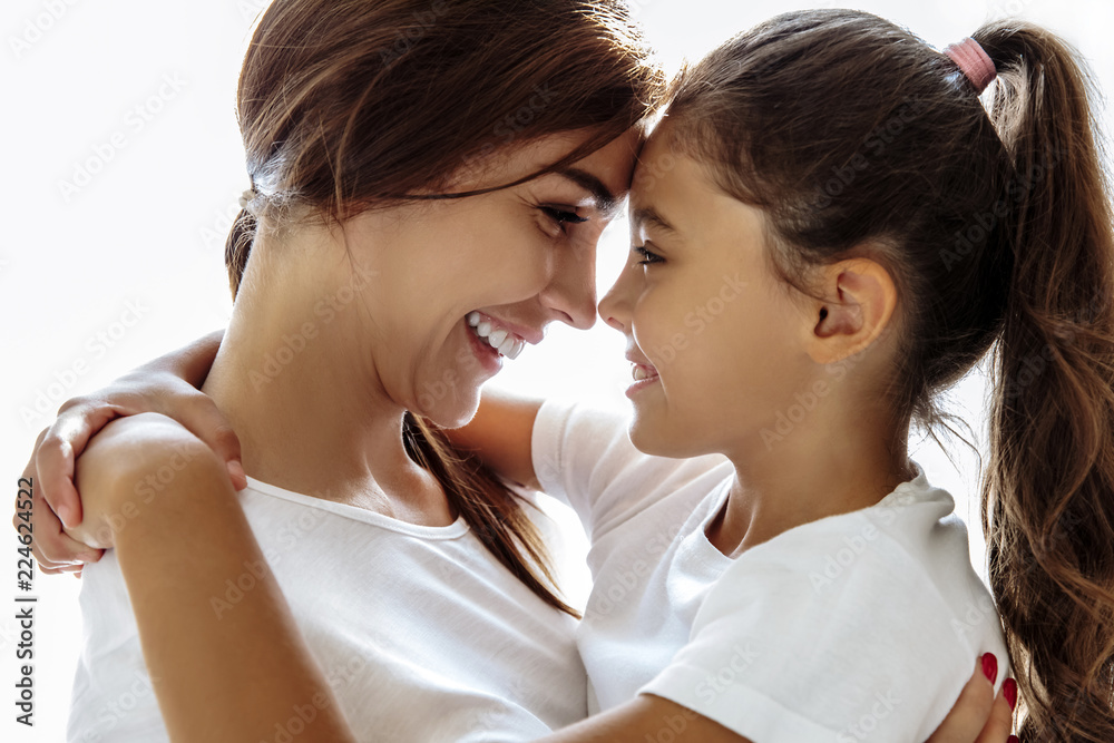 Family. Love. Togetherness. Mom and daughter are hugging, touching with their foreheads and smiling; at home