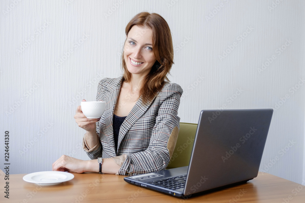 Cute young female adult working on laptop computer at desk next to coffee cup Cute young female adult working on laptop computer at desk next to coffee cup
