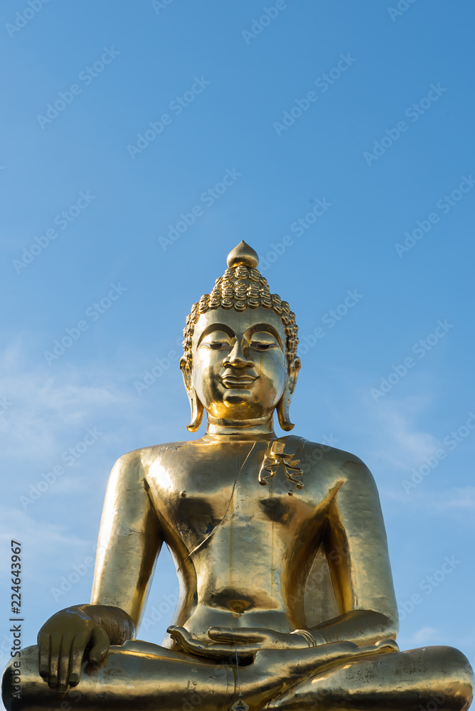 From below shot of golden shiny statue of Buddha in sunlight on background of blue sky