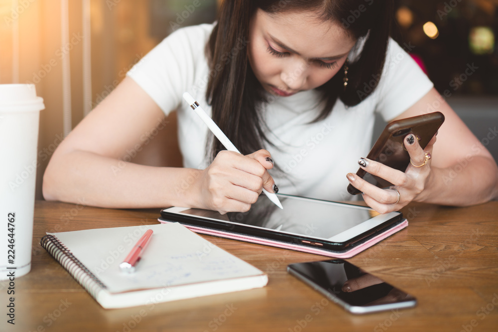 Young asian woman graphic designer using digital tablet, touch pen, smartphone on wooden table at cafe. Young asian woman graphic designer using digital tablet, touch pen, smartphone on wooden table at cafe.