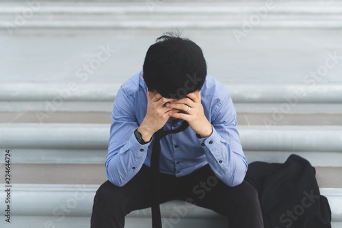 Young asian businessman sitting on concrete stairs and holding head with hand are stressed with work and life issues. He thinks to commit suicide when he know business is failing and unemployed.