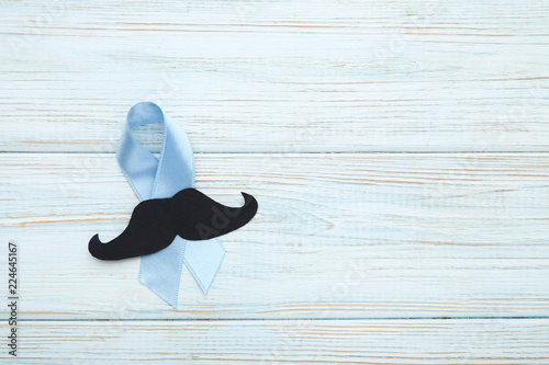 Blue ribbon with paper mustache on wooden table. Prostate cancer concept