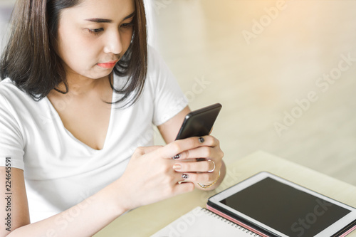 Beautiful asian woman reading message on smartphone while sitting at table in office.