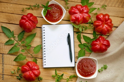tomato ketchup.Tomato sauce.The recipe for ketchup. home made sauce ketchup in white plates, large ripe red tomatoes with leaves, basil, marjoram and an empty notebook on a wooden table.