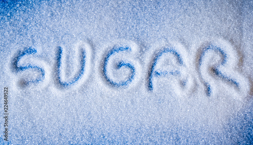 The word sugar write on a pile of white sugar with blue background