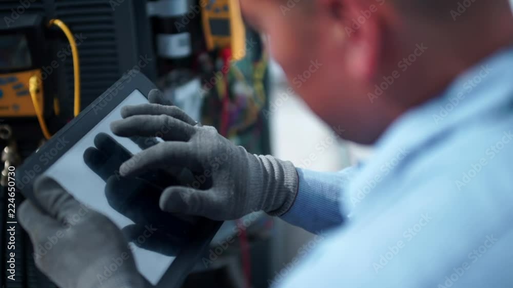 Male HVAC technician uses an ipad tablet while working and fixing an air conditioning unit outside.