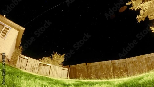 NIGHT LAPSE - Stars in the sky filmed in the yard of a house with bright green grass and a full wooden fence. photo