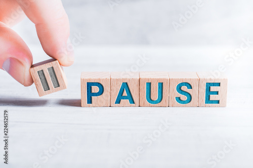 The Word Pause Formed By Wooden Blocks And Arranged By Male Fingers On A White Table photo