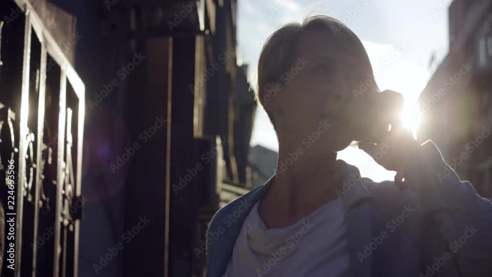 Beautiful midd-age woman recives call on the street with sunshine in background Beautiful midd-age woman recives call on the street with sunshine in background