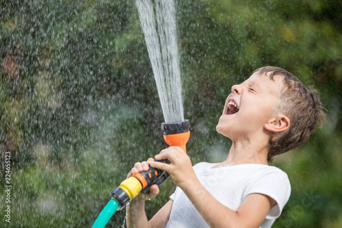Happy little boy pouring water from a hose.