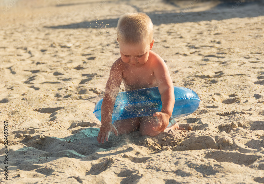 Blonde boy playing with sand on sunny hot beach Blonde boy playing with sand on sunny hot beach
