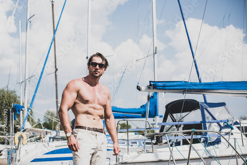 Sexy bearded man standing on the yacht club. Guy on a sailing boat. Handsome man enjoying life, traveling on yacht along beautiful Europe, guy with fit sexy body modeling, summer vacation 