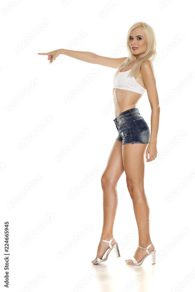 Young pretty woman posing in short jeans on white background, and pointing on empty space