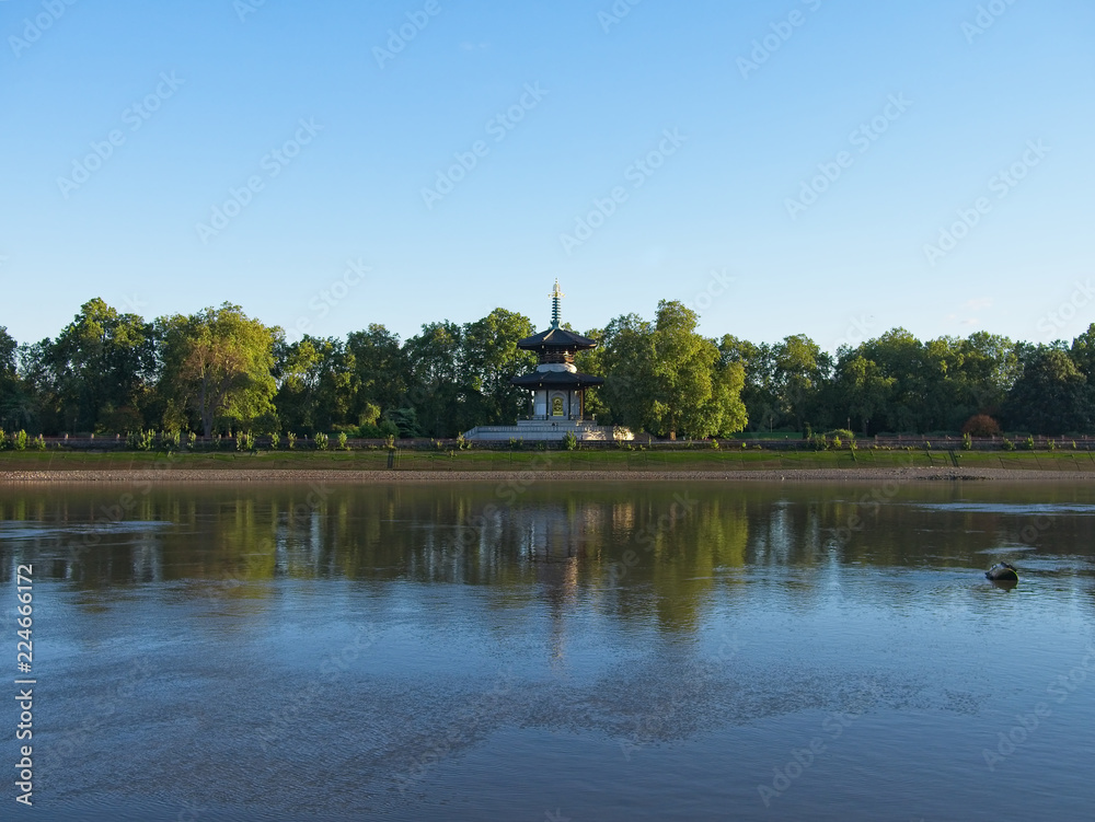 Thames river and Battersea Park in London, England. Beautiful green trees against blue sky. The Peace Pagoda is seen in the park.