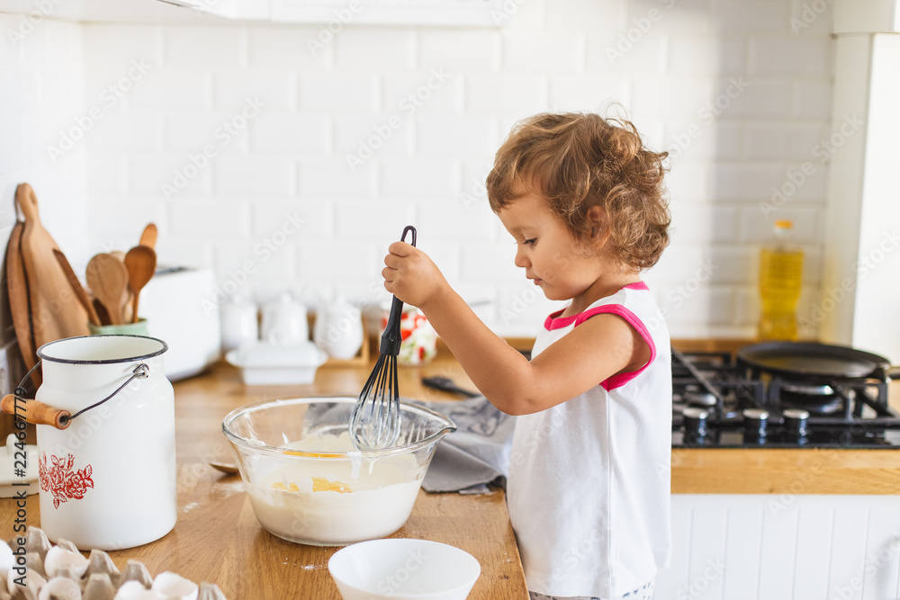 3 years cute girl preparing dough for pancakes at the kitchen.