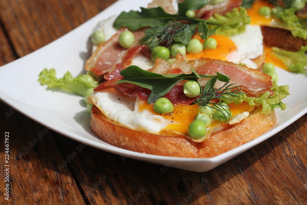 Bruschetta with rucola, chrispy bacon, green pea and poached egg served on white plate Bruschetta with rucola, chrispy bacon, green pea and poached egg served on white plate
