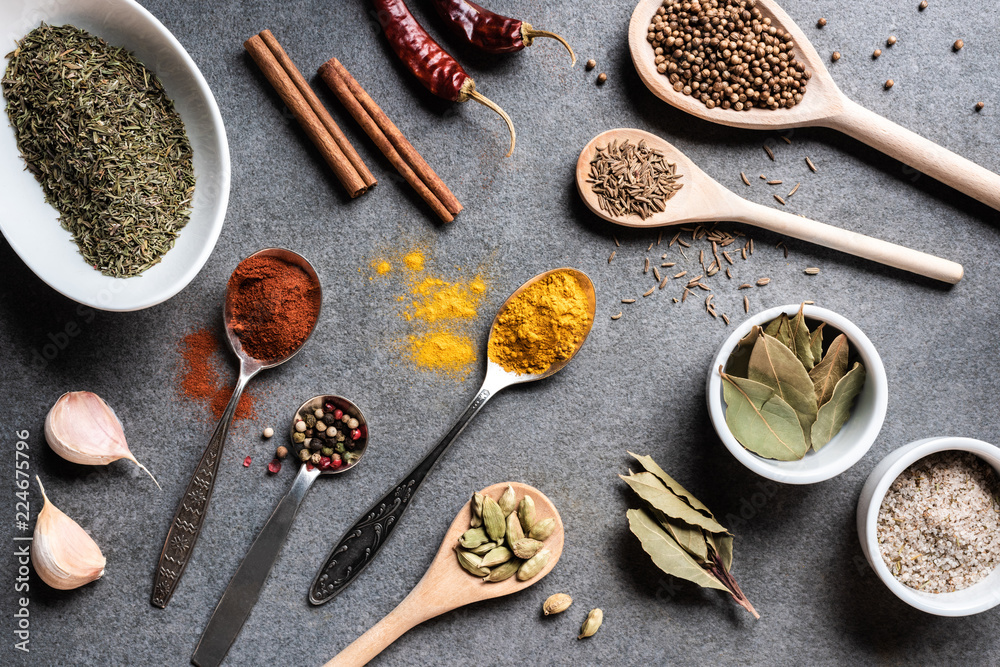 top view of various aromatic dried spices in bowls and spoons on grey surface
