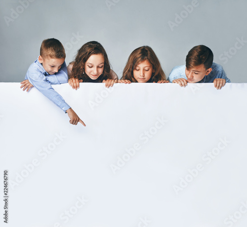 a Four children holding a big billboard, looking down on it.