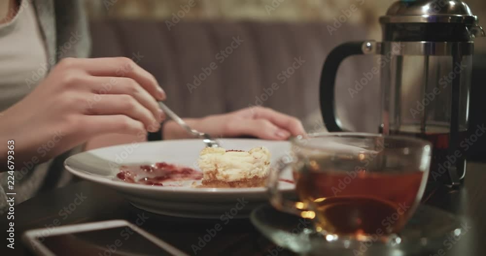 Attractive young woman eats an appetizing cake and drinks aromatic tea in the cafe. Close up. Attractive young woman eats an appetizing cake and drinks aromatic tea in the cafe. Close up.
