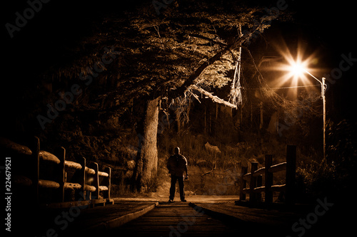 Night stalker concept. Man standing on wood bridge under street light in dark night photo