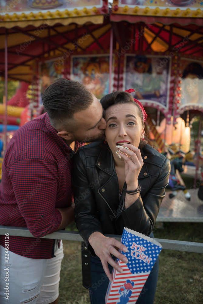 young man surprise kissing woman in amusement  park while she's eating pop corns 